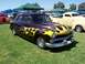 2002 Ford Mustang - A custom hot rod with flame graphics is displayed at an outdoor event with other vehicles and tents.