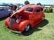 2002 Ford Mustang - A bright red hot rod sedan is displayed with its hood open at an outdoor car show.
