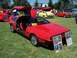 2002 Ford Mustang - A red DeLorean DMC-12 is displayed with its iconic gull-wing doors open at an outdoor car show.