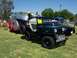 2002 Ford Mustang - A vintage Willys Jeep is hitched to a teardrop trailer carrying a boat, with a police car visible in the background.