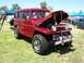 2002 Ford Mustang - Vintage red station wagon SUV parked on grass with hood open, other vehicles and tents in background.