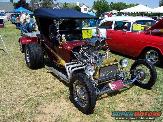 Maroon hot rod with a V8 engine, chrome accents, and a black convertible top parked on grass