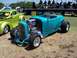 2002 Ford Mustang - A turquoise hot rod and a green custom pickup truck are parked outdoors at an event with a band on a trailer in the background.