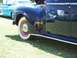 2002 Ford Mustang - Reflections on the polished surface of a dark vintage car reveal other vehicles and tents at an outdoor gathering.