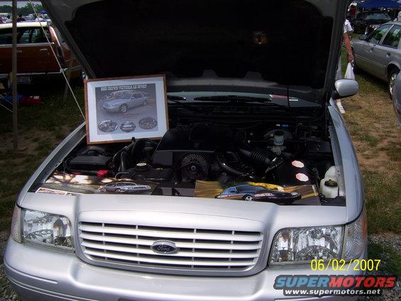 Silver 2003 Ford Crown Victoria engine bay, hood open, with a framed display and model car