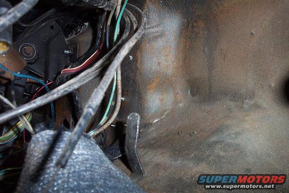 Close-up of rusty metal firewall with tangled wires and brake/clutch pedals