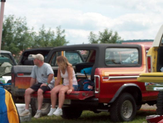 1978 Ford Bronco with two people sitting on its tailgate, parked next to another vehicle