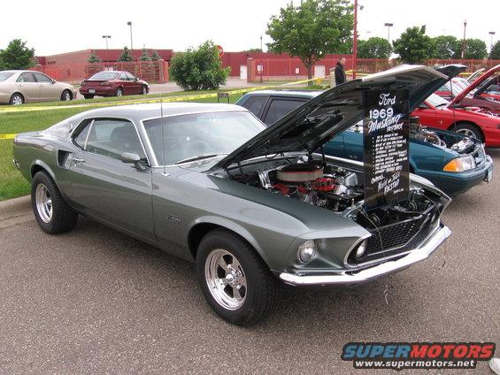Gray 1969 Ford Mustang with hood open, showing engine. Chrome wheels and trim. Parked outdoors