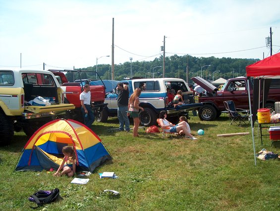 White and blue 1978 Ford Bronco with open tailgate, people relaxing nearby