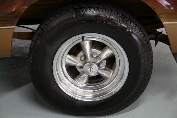 Chrome five-spoke wheel with a black tire on a vehicle with wood paneling