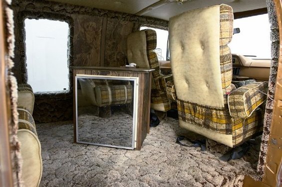 Interior of a van with shag carpet, plaid seats, and a small refrigerator