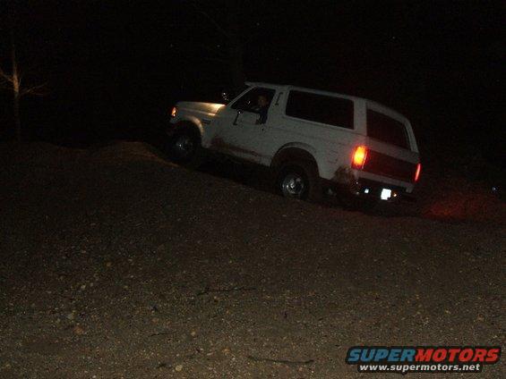 White SUV driving up a dirt hill at night, rear taillights illuminated