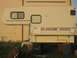 1996 Dodge 2500 - A side view of a truck camper parked in front of a brick building, resting on makeshift supports.