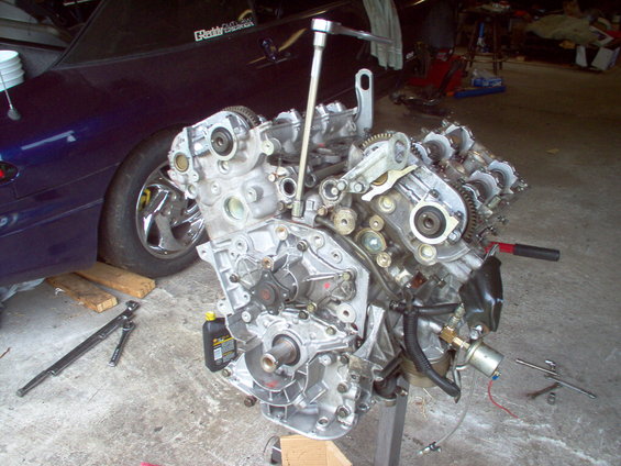 Engine on a stand in a garage, with a dark blue car in the background