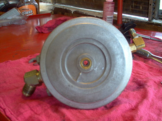 Circular metal part with brass fittings on red cloth, tools nearby