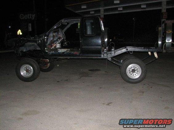Black truck chassis with removed body panels, exposed interior, and large wheels