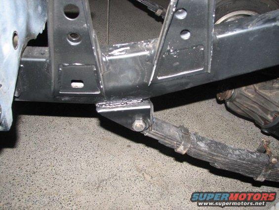 Close-up of a leaf spring attached to a frame bracket, with part of a differential visible