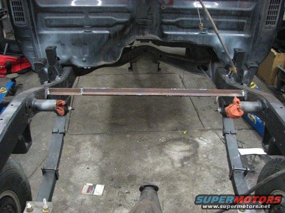 Truck frame with leaf springs and suspension components visible. A metal bar is welded across the frame