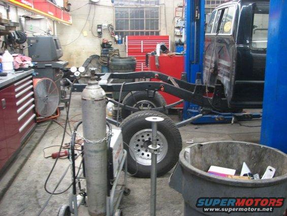 Truck chassis and cab on a lift in a garage, with welding equipment nearby