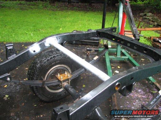 vehicle frame with leaf springs and a tire visible, on a stand outdoors