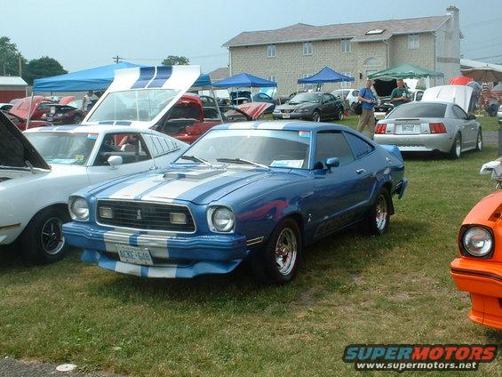 Blue 1978 Ford Mustang II with white racing stripes parked on grass, license plate ACKE-648
