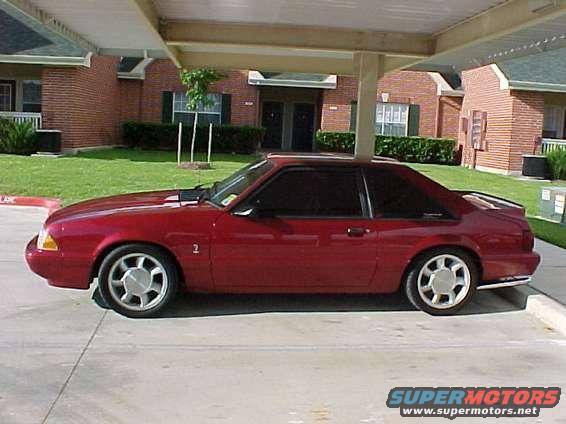 Red coupe with tinted windows and a rear spoiler parked under a carport