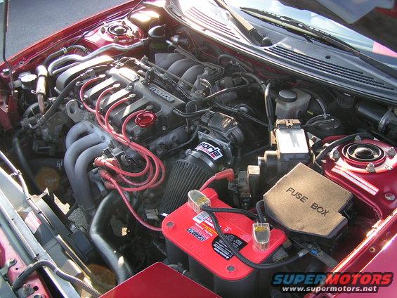 Engine bay with red battery, fuse box, and Mazda engine