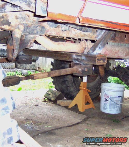 Orange vehicle frame on jack stands, showing rusted suspension and exhaust pipe