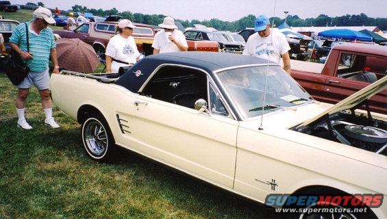 Cream 1965 Ford Mustang coupe with black vinyl top, hood open, people standing around it
