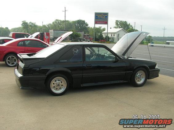 Black coupe with hood open, side view, aftermarket wheels, spoiler, and a graphic on the rear window