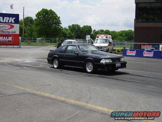Black 1988 Ford Mustang on drag strip with ambulance in background