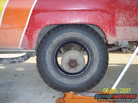 Red SUV rear wheel with 'Mud Terrain Procomp' tire, jack visible