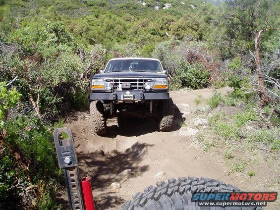 Black Ford Bronco on a dirt trail, front view. Modified bumper with winch, large off-road tires