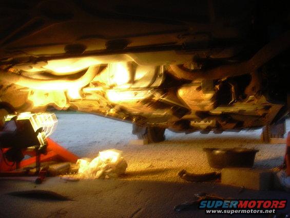 underside of a car on jack stands with tools and a drain pan below