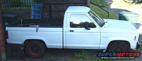 White pickup truck, side view, parked outdoors with red-rimmed wheels