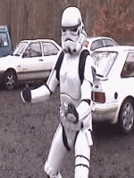 Person in a Stormtrooper costume giving a thumbs up, with cars in the background
