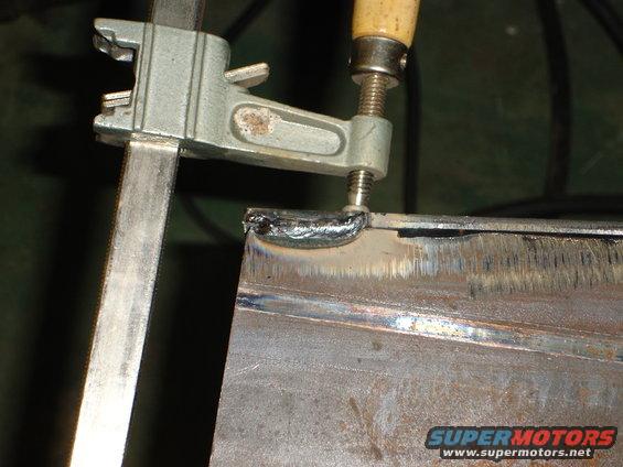 Clamp holding metal for welding, SuperMotors logo visible