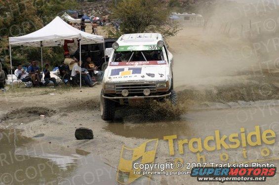 Off-road race truck with number 301 on windshield splashing through mud puddle. Modified front end with large tires