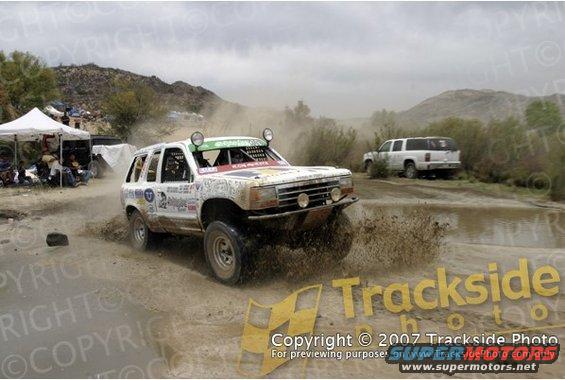 Off-road race truck splashing through mud, another SUV in background
