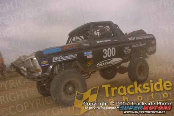 Black off-road race truck with number 300, modified body, large tires, and roll cage, kicking up dust