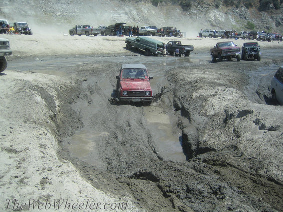 Red 1987 Suzuki Samurai driving through mud
