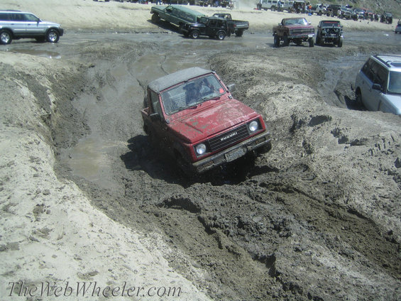 Red 1987 Suzuki Samurai driving through mud