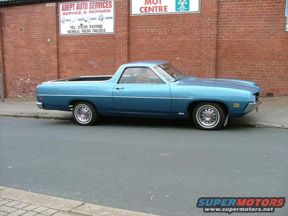 Blue 1970 Ford Ranchero parked curbside, with 'ADEPT AUTO SERVICES' sign on brick wall behind it