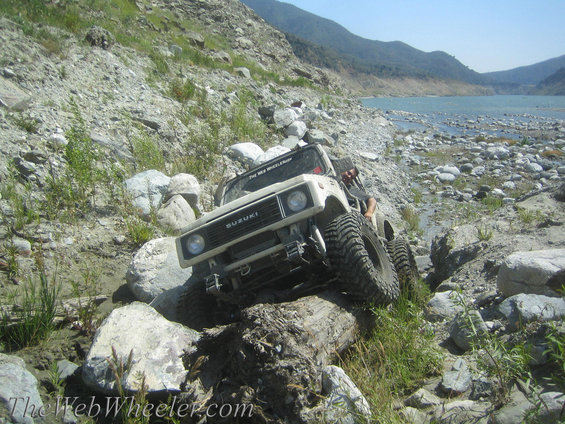 White 1987 Suzuki Samurai navigating rocky terrain near a body of water