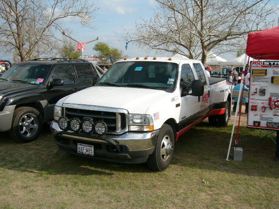 White Ford F-350 dually pickup truck with aftermarket lights and red trim. Black SUV parked to the left. MSD display to the right