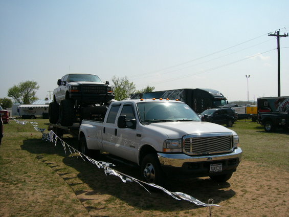 White Ford F-350 dually towing a lifted white Ford F-Series truck on a trailer. License plate reads TKN-C31