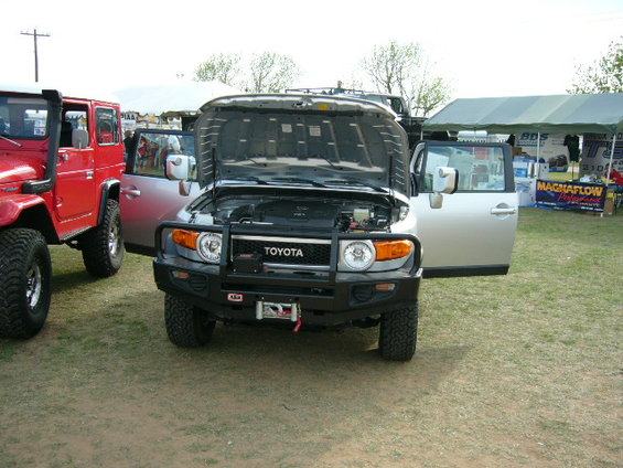 Silver Toyota FJ Cruiser with hood open, parked next to a red Jeep-like vehicle. ARB bumper and winch visible