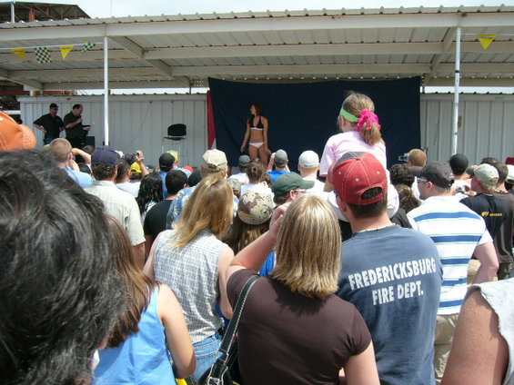 Crowd watches a woman in a bikini on a stage at an outdoor event