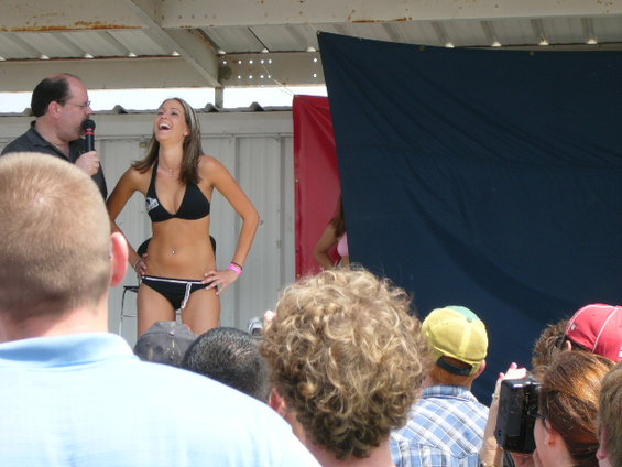 Woman in black bikini laughing on stage with a man holding a microphone