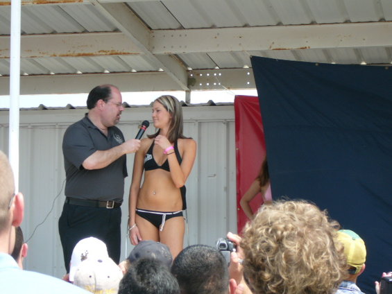 Woman in black bikini on stage with interviewer, crowd in foreground